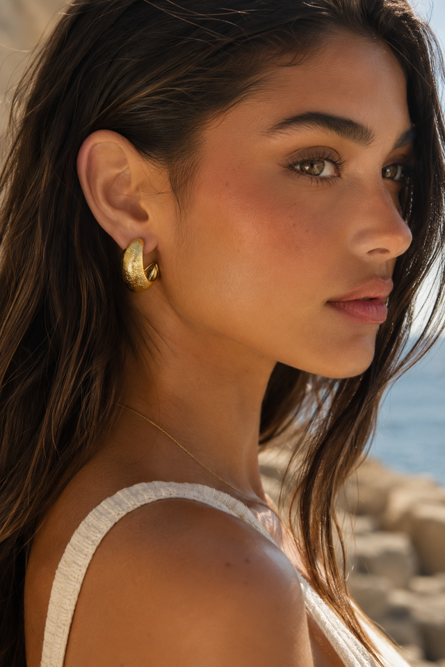 Femme portant les boucles d’oreilles bombées dorées Lumé dans un décor méditerranéen