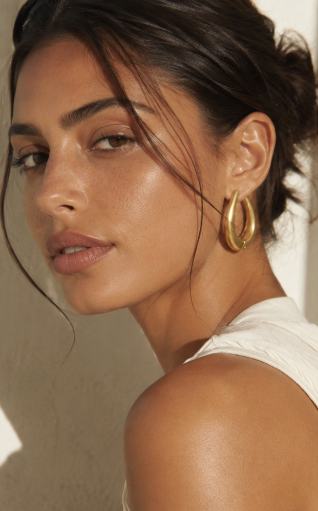 Femme portant des boucles d’oreilles goutte sculptée couleur or
