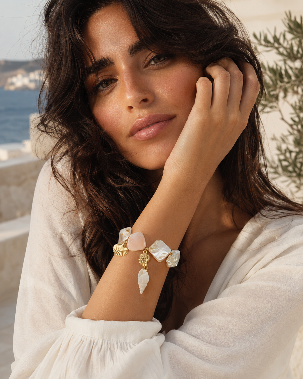 Femme méditerranéenne portant le bracelet coquillages nacrés à breloques Lumé dans un décor lumineux